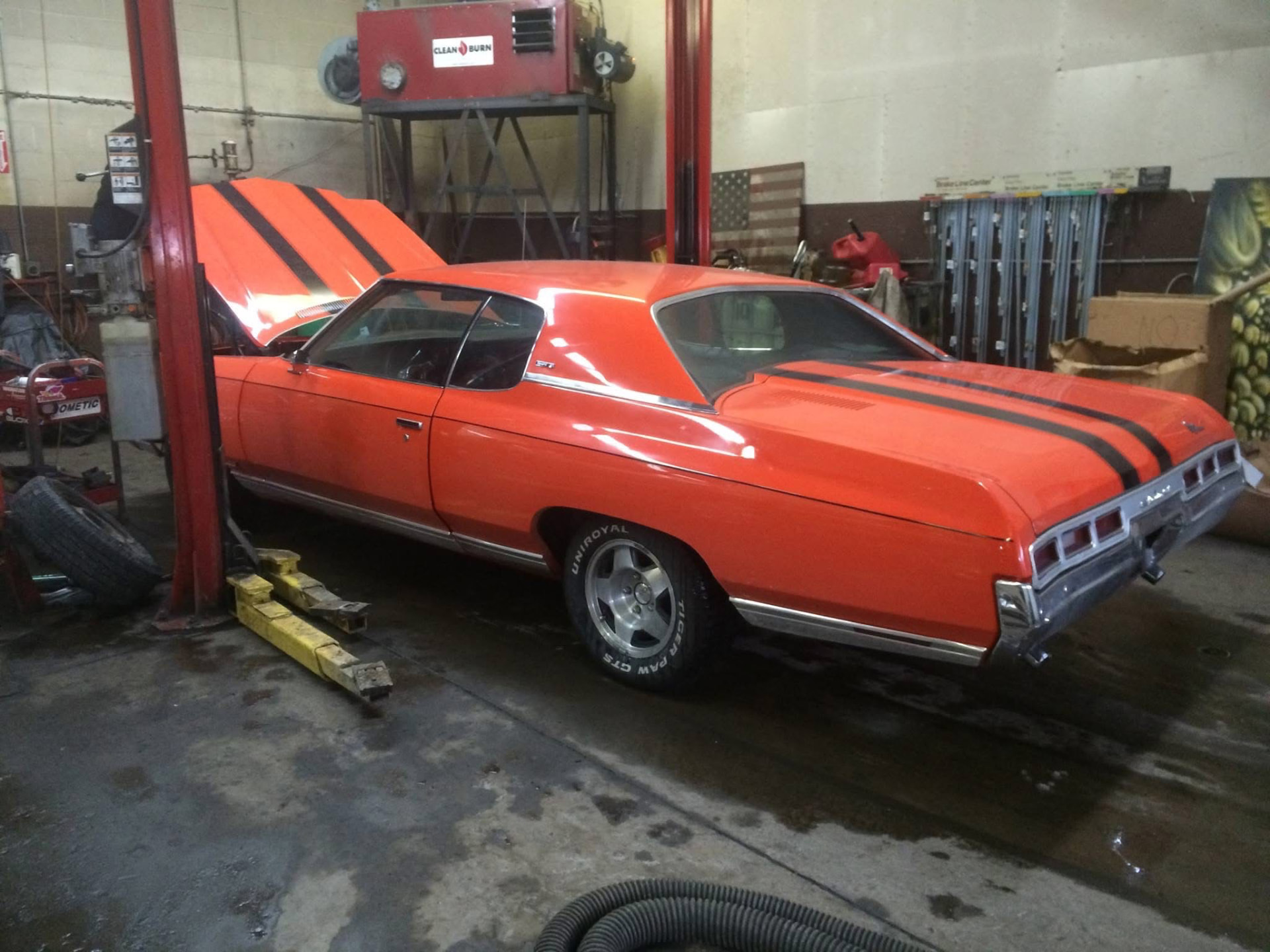Orange classic Chevrolet with black stripes raised on a lift at Sam's Auto by CUBI